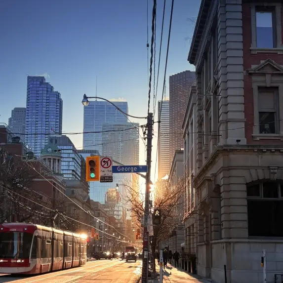 A Toronto street at sunrise with a streetcar, traffic lights, and tall buildings in the background. A George Street sign is visible.