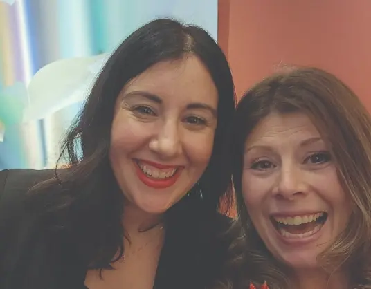 Two coworkers smiling close together for a selfie indoors.