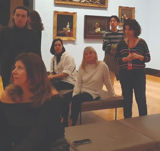 A group of people gathered in an art museum gallery, with framed paintings on the walls behind them.