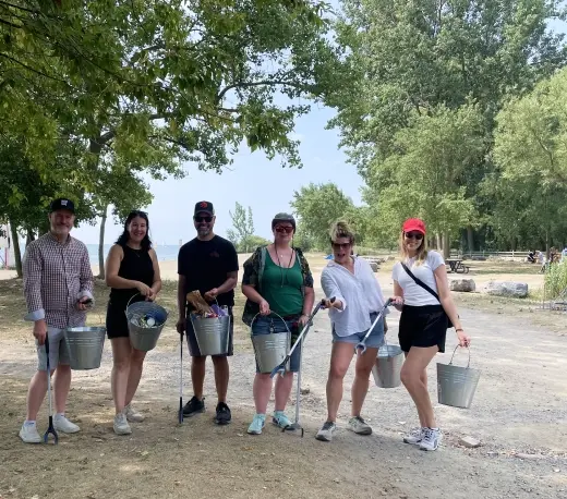 Volunteers standing on a tree-lined path holding buckets and litter pickers after a trash cleanup.