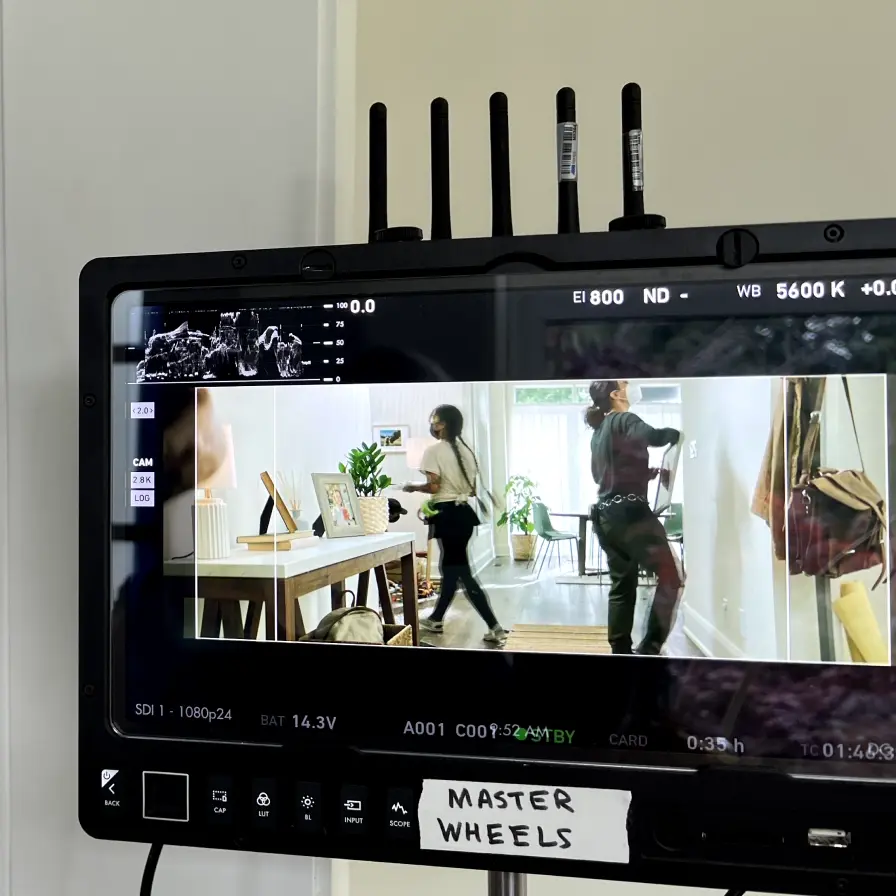 A monitor displays a scene from a video production with two people walking through a bright room; MASTER WHEELS is labeled below the screen.