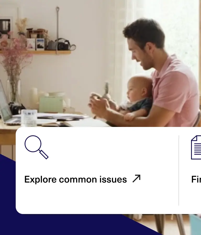 A snapshot of a webpage. A man sits at a desk holding a baby while working on a laptop in a bright, cozy home office.