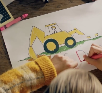 Child drawing a yellow excavator with crayons on paper.
