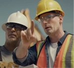 Two construction workers in hard hats and safety gear reviewing a work site.