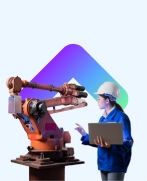 Engineer in a hard hat operating a laptop beside an industrial robotic arm.