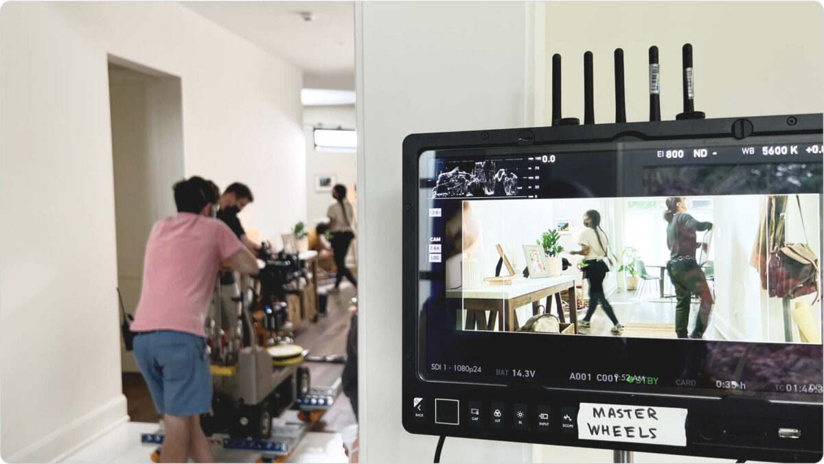 Interior of a house where a film crew is moving a camera and a nearby screen shows footage