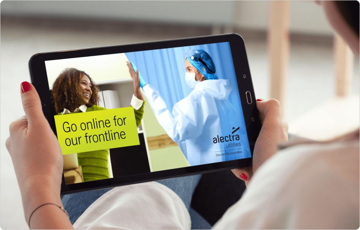A woman sits while looking at a tablet displaying two images of frontline workers with the words: ‘go online for our frontline’.